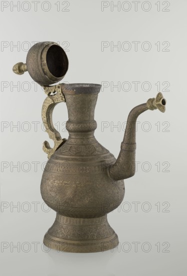 Jug aftabe, aftabe, geometric and plant ornament, dragons, zoomorphism; Decoration: dense plant and geometric ornament. Persian, Qajar dynasty 1785–1925, 19th century. Materials/medium: vessel. Place of origin: Iran possibly Central Asia. Dimensions: height 34.0 cm, width 22.7 cm, diameter 13.3 cm., A metal ewer with an ornate hinged lid and curved spout sits against a pale background; the vessel displays intricate engraved patterns across its bulbous body, flared neck, and round pedestal base, with a decorative handle that connects the lid to the body; the metal appears in tones of muted bronze and brass with darker brown areas and some lighter golden highlights, and the lid interior is visibly darker.