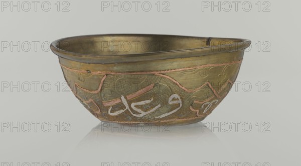 Bowl, Islamic art, Arabic culture, arabesque ornament, calligraphy, Arabic inscriptions, geometric motifs, 19th century, Middle East, possibly Syria, vessel, height 4.9 cm, diameter 13.3 cm, A shallow metal bowl sits against a pale gray background, shown in a frontal view with its interior visible; the bowl has a warm brass color with areas of darker patina and a few copper-colored inlaid lines forming decorative shapes, and parts of its surface show a slightly textured, hammered appearance; there are traces of a pale grayish-white material in curved strokes on the exterior decoration, and the rim is slightly darker with subtle wear; the bowl rests on a reflective surface that creates a faint mirrored reflection beneath it.