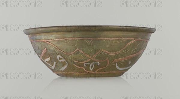 Bowl, Islamic art, Arabic, arabesque ornament, calligraphy, Arabic inscriptions, geometric motifs, 19th century, Middle East, possibly Syria; vessel, height 4.9 cm, diameter 13.3 cm, A shallow metal bowl shown from the side with a rounded rim and a gently tapered body, decorated with an incised pattern of curved and angular motifs highlighted by inlaid bands; the surface shows a mottled metallic finish in shades of olive green and brass with accents of copper and traces of whitish markings, set against a pale neutral background.