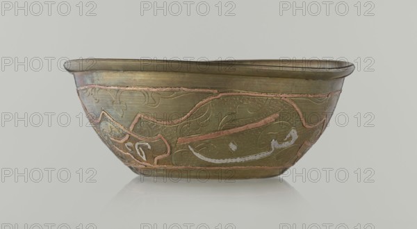 Bowl, Islamic art, Arabic culture, arabesque ornament, calligraphy, Arabic inscriptions, geometric motifs, 19th century, Middle East possibly Syria, vessel, height 4.9 cm, diameter 13.3 cm, A shallow metal bowl displayed against a pale gray background, showing an exterior with a warm brass tone and a few areas of muted copper inlay forming flowing decorative lines; the bowl has a rounded rim with a slightly darker brass band, and the body features an embossed texture with swirling, curvilinear patterns highlighted by soft pinkish copper accents and a few pale silvery-white inlaid strokes; the underside and interior edges show subtle variations of olive-brown and darker bronze, and the bowl rests on a reflective pale surface that creates a faint mirror image.