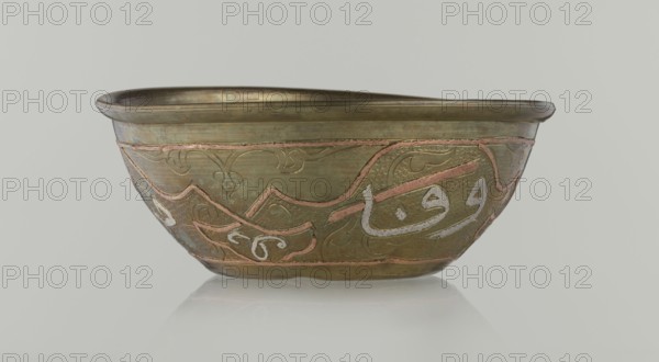 Bowl, Islamic art, Arabic culture, arabesque ornament, calligraphy, Arabic inscriptions, geometric motifs, 19th century, Middle East, possibly Syria, vessel, height 4.9 cm, diameter 13.3 cm, A metal bowl with a wide rim and curved sides sits on a reflective surface, showing a group of decorative inlaid lines and shapes around its exterior. The bowl's surface is primarily a muted greenish-bronze color with visible areas of warm coppery pink inlaid accents and pale silvery-white elements. The decoration includes flowing curved bands, scalloped motifs, and textured stippled sections, all following the contour of the bowl. The rim and interior display a slightly darker bronze tone, and the overall finish shows subtle variations and patina in greenish, bronze, coppery, and silvery hues.