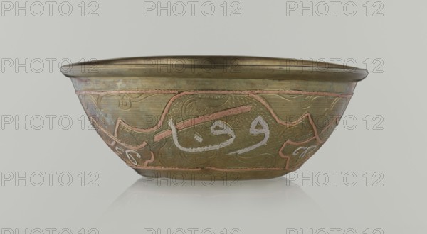Bowl, gift, Islamic art, Arabic culture, arabesque ornament, calligraphy, Arabic inscriptions, geometric motifs, 19th century, Middle East, possibly Syria, vessel, height 4.9 cm, diameter 13.3 cm, A shallow metal bowl with a rounded rim sits against a pale gray background; the bowl shows a predominantly brass-colored surface with areas of darker and lighter patina, and it is decorated with a band of raised curving designs in a pinkish tone and a few pale silvery accents; the body of the bowl has textured hammered areas and smooth sections, with ornamental flowing motifs in subtle engraved lines; the rim and base edges are slightly darker brass, and the overall color palette includes brass, pinkish copper, pale silver, and muted greenish-brown tones.