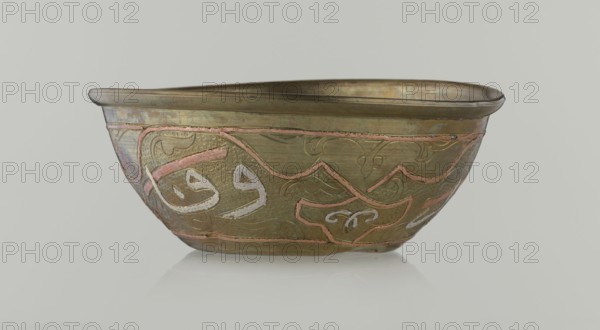 Bowl, Islamic art, Arabic, arabesque ornament, calligraphy, Arabic inscriptions, geometric motifs, 19th century, Middle East, possibly Syria, vessel, height 4.9 cm, diameter 13.3 cm, A shallow metal bowl with a slightly irregular rim sits on a pale background; the bowl shows a metallic base color of aged brass with visible areas of darker patina and subtle iridescent greenish and bluish tones, plus pinkish inlaid bands and pale silvery-white inlaid decoration. The exterior surface features textured hammered patterns and raised curving lines forming ornamental motifs, with a few areas of smoother metal near the rim and subtle surface wear. The image shows the bowl in profile, reflecting softly on the surface beneath it, and the overall color palette includes brass, greenish-blue, pink, silvery-white, and areas of darker brownish patina.