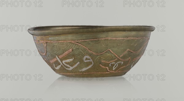 Bowl, Islamic art, Arabic culture, arabesque ornament, calligraphy, Arabic inscriptions, geometric motifs, 19th century, possibly Syria, vessel, height 4.9 cm, diameter 13.3 cm, A shallow metal bowl with a rounded rim sits against a pale gray background, showing a greenish-brass surface with areas of pinkish and silvery inlay. The bowl's exterior features decorative raised and incised patterns with flowing curves and textured hammered areas, incorporating bands of pinkish metal and silvery highlights. The rim appears slightly darker brass, while the interior edge shows a muted green-brown tone. The bowl rests on a reflective surface that creates a soft near-white reflection beneath it.