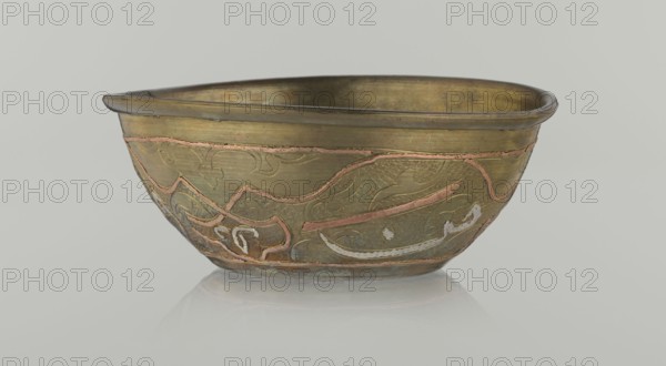 Bowl, Islamic art, Arabic culture, arabesque ornament, calligraphy, Arabic inscriptions, geometric motifs, 19th century, Middle East possibly Syria, vessel, height 4.9 cm, diameter 13.3 cm, A shallow metal bowl with a rounded rim sits on a pale neutral surface, displaying a warm brass tone overall with areas of darker patina and subtle greenish aging; decorative inset bands and raised patterns in a reddish-copper color trace flowing, curving motifs around the exterior, and there are a few lighter silvery-white highlights within some decorative areas; the interior shows a darker brass-golden surface with slight variations in tone, and the background is a soft light gray.