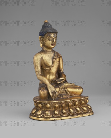 Shakyamuni Buddha, buddha iconographic, lotus throne iconographic, Himalayan culture, Tibetan Buddhist art, Buddha ca. 560–480 BCE, ushnisha, mudras, 19th century, Tibet, sculpture; height 10.2 cm, width 7.3 cm, depth 5.4 cm, A gilded statue seated on an ornate base, shown against a plain gray background; the figure has a gold-colored body with a darker blue hair area topped with a small gold point, a serene facial expression, one hand resting on the knee and the other held near the lap, draped clothing with visible folds, and the base features repeated petal-like motifs in gold with areas of darker tarnish and wear.