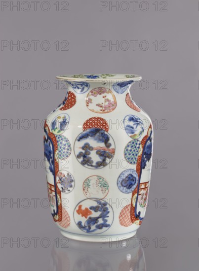 Vase, Tashiro maker/firm, Japanese, colored porcelain, ceramics, Meiji period 1868–1912, 2nd half of 19th century, Hizen, Arita, Japan. Figurative scenes with landscape background including peonies, camellias, wisteria, fish, pine trees; asanoha pattern. Vessel vase, height 28.5 cm, diameter 19.0 cm., A white ceramic vase with a flared rim and rounded shoulders sits against a plain gray background; the vase is decorated with a pattern of circular medallions and geometric panels in colors including blue, red, green, pink, orange, and gold, featuring floral motifs, stylized foliage, and abstract shapes, with areas of solid blue brushwork and red lattice patterns, and the base of the vase shows a thin blue line and a subtle reflection on the surface beneath it.