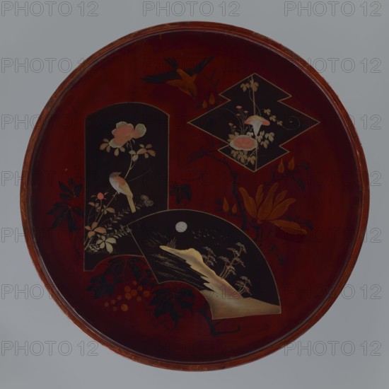 Tray, Meiji 1868–1912, Japanese art, Japanese culture; iconography: wisteria, kachôga flowers and birds, pines, moon, fans, bridge; early 20th century Meiji Period, Japan; vessel; height 2.8 cm, diameter 42.0 cm, A round shallow tray with a dark reddish-brown surface and a thin rim shows a decorative scene inlaid with lighter and darker panels; a tall arched dark panel contains a perched small bird among pale pink and cream flowers and leaves, a geometric dark panel above holds pale floral motifs, and a fan-shaped dark panel at the bottom depicts a pale landscape with a moon and stylized plants; surrounding these panels are additional floral and leaf motifs in shades of orange, brown, cream, and dark green.