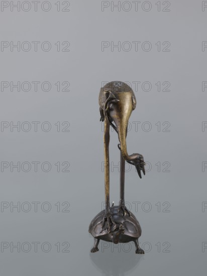Candlestick shokudai, lotuses, Genius, turtles, cranes iconography, Japanese art, Meiji 1868–1912, animals, 2nd half of the 19th century, Japan, candlestick, height 37.0 cm, A metallic sculpture in shades of bronze and dark brown shows a bird-like figure with long, thin legs standing on the back of a turtle-like creature; the bird has a rounded head with textured surface and a downward-curving beak, one wing or appendage draping along its side, and a hooked talon visible near the lower part of its body, while the turtle has a domed shell, short stout legs, and a small head projecting forward; the background is a smooth light gray.