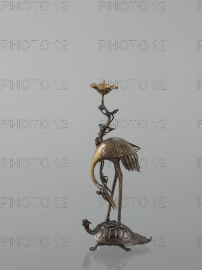 Candlestick shokudai, lotuses, turtles, cranes iconography, Japanese art, Japanese, Meiji 1868–1912, animals, 2nd half of the 19th century, Japan, candlestick, height 37.0 cm, A metallic sculpture showing a standing bird with a curved neck and textured wings perched on the back of a turtle, the bird supported by a slender vine-like stem that rises to a flower-shaped cup at the top; the piece displays metallic tones of bronze and gold with darker brown and black areas, and sits on a pale gray background with a subtle reflection beneath it.