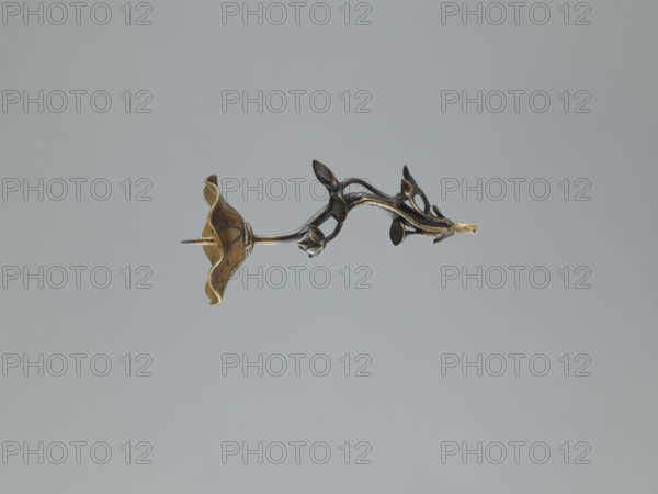 Candlestick shokudai, lotuses, turtles, cranes iconography, Japanese art, Meiji 1868–1912, animals, 2nd half of the 19th century, Japan, candlestick, height 37.0 cm, A metallic object shaped like a stylized flowering vine floats against a pale gray background, showing a curled petal-like form at one end in a warm golden color with darker brownish accents and a thin pointed projection, while the stem and branching elements display darker bronze and black tones with small rounded leaf-like shapes and a few lighter golden highlights.