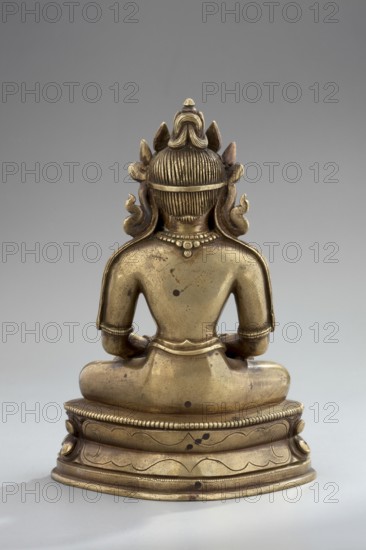 Amitayus, Himalayan/Tibetan Buddhist and Chinese art influences, lotus throne iconography, Buddha Amitayus seated on a lotus or vajra throne holding a vase of long life, 18th–19th century, possibly China or Mongolia, figurine sculpture and cult object, height 11 cm, width 7.8 cm, depth 5.5 cm., A metallic statue shown from the back, seated on a rounded decorative base, with a smooth gold-toned surface and areas of darker patina and small dark spots; the figure has stylized hair tied in a bun and flanked by carved ornamental shapes, a simple necklace around the neck, bare shoulders and arms with wristbands, and a cloth or belt around the waist, all rendered in gold and darker brownish-gold tones against a neutral gray background.
