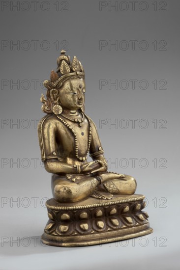 Amitayus, Tibetan Buddhist/Himalayan and Chinese art influences, lotus throne, Buddha Amitayus holding a vase of long life, seated lotus or vajra posture, 18th–19th century, possibly China or Mongolia, figurine sculpture and cult object; height 11 cm, width 7.8 cm, depth 5.5 cm., A seated metallic statue on an ornate base, shown against a plain gray background, with a golden-bronze surface that shows variations of darker tarnish and lighter highlights; the figure wears a decorative crown with petal-like elements and a small pointed finial, has stylized hair and large circular earrings, and displays a calm facial expression with closed or downcast eyes and a raised mark on the forehead. The torso is adorned with layered beaded necklaces and armlets, and the arms rest in the lap with hands arranged in a meditative gesture. The clothing details include patterned bands around the legs and a draped element over one shoulder. The rounded base beneath the figure features a repeating petal mot...