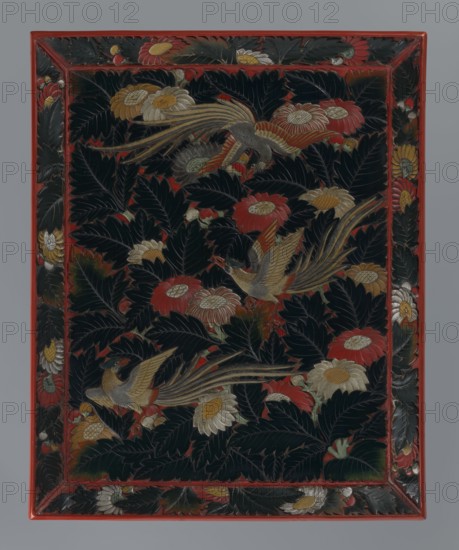 Tray made of red and dark green lacquer; decoration: three hôô phoenix birds among chrysanthemum flowers and leaves, made using the maki-e dusting technique on black lacquer with small accents in white and yellow. Japanese, Meiji period 1868–1912, 19th/20th century. Tray, height 3.0 cm, width 45.5 cm, depth 36.7 cm., A rectangular panel with a red frame encloses a dark background filled with large dark green leaves, several red flowers, and several pale yellow and cream flowers; three stylized birds with long striped tails in shades of gold, brown, and gray appear among the foliage, and small touches of orange and muted green accent leaves and petals throughout.