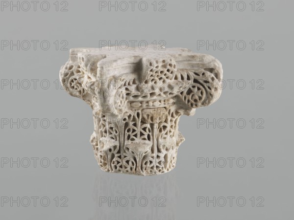 Column capital from Madinat az-Zahra, Islamic art, Arabic art, Arabic culture, Caliphate of Córdoba 929–1031, Al-Andalus, architectural element capital with acanthus ornament, 10th century, Madinat az-Zahra, Al-Andalus; height 22.3 cm, width 23.3 cm, depth 24.0 cm, weight 15.5 kg., A carved stone object with intricate openwork and lattice-like patterns, showing floral and foliate motifs and rounded volute forms, in shades of white, off-white, beige, and light gray set against a uniform light gray background.