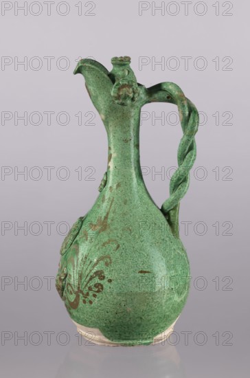 Jug, Islamic, Turkish, Ottoman dynasty 1299–1922, glazed ceramic, 19th century, Çanakkale, Turkey; floral ornament; braided handle; with a filter; curved spout; neck cover with a rosette; height 34 cm, diameter 16.2 cm., A green ceramic jug with a rounded body tapering into a narrow neck and a spouted top, featuring a twisted handle attached from near the rim down to the shoulder; the surface shows darker green speckling and patches of brownish discoloration, and there is a decorative raised motif on the body.
