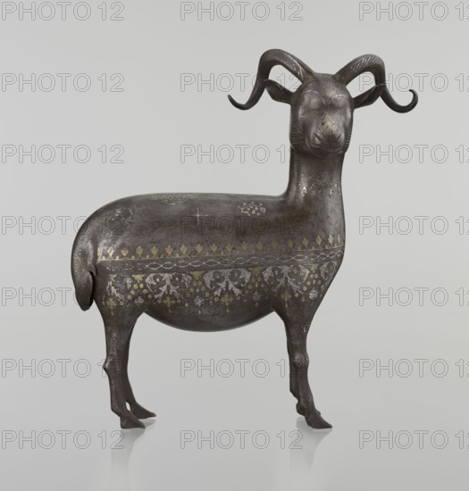 Ram; maker, Persian, Qajar dynasty 1785–1925; 1st half of the 19th century; sculpture, animal figurine ram; decorated on the back with medallions and palmettes with floral ornament; materials/technique: Islamic art; dimensions: H 22.5 cm, W 20.5 cm, D 9.0 cm; weight 0.64 kg., A sculpted animal figure with curved horns standing on four slender legs, rendered in a dark metallic gray with areas of lighter gray wear and subtle brownish patina; its body is decorated with patterned bands and motifs in muted gold and silver tones, including floral and foliate designs along the midsection and small decorative marks on the back and neck; the horns are darker and slightly glossy, the face is smooth with faint incised lines, and the overall surface shows a mix of matte and slightly reflective textures against a pale neutral background.