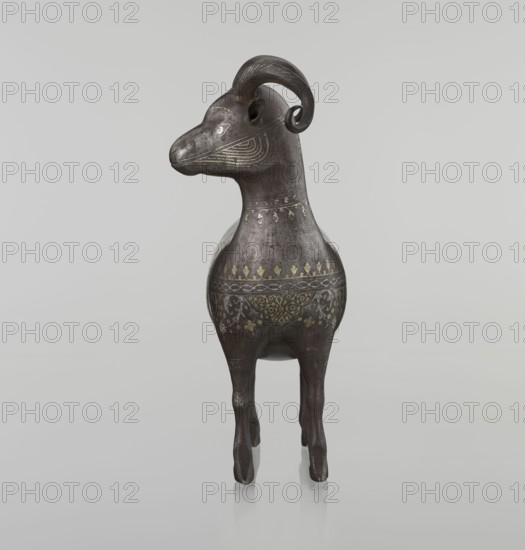 Ram, Islamic art, Persian culture, Qajar dynasty 1785–1925, sculpture, animal figurine of a ram with horns, decorated on the back with medallions and palmettes with floral ornament, geometric motifs, 1st half of the 19th century, Iran, height 22.5 cm, width 20.5 cm, depth 9.0 cm, weight 0.64 kg, A sculpted animal figure standing on four slender legs with a rounded body and an elongated neck, rendered in dark brown and black tones with a slightly metallic sheen; the head has curved horns and a pronounced snout, with decorative curved line patterns on the face in a muted gold or yellow color; the body is decorated with bands of floral and geometric motifs in muted gold and pale gray, and there are subtle worn or distressed patches showing lighter brown areas; the background is a smooth, very light gray, and the figure casts a soft reflection on the surface beneath it.