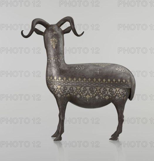 Ram, Islamic art, Persian, Qajar dynasty 1785–1925, sculpture; animal figurine of a ram with horns; decorated on the back with medallions and palmettes with floral ornament; geometric motifs and floral ornament; 1st half of the 19th century, Iran; height 22.5 cm, width 20.5 cm, depth 9.0 cm, weight 0.64 kg., A sculpted animal figure resembling a ram with curved horns stands on a smooth pale gray background; the figure is primarily dark brown to black with metallic gold decorative patterns across its body and neck, and there are areas of lighter gray patina on its surface; the horns are dark brown, the legs are the same dark shade, and small highlights reflect a slightly glossy finish.