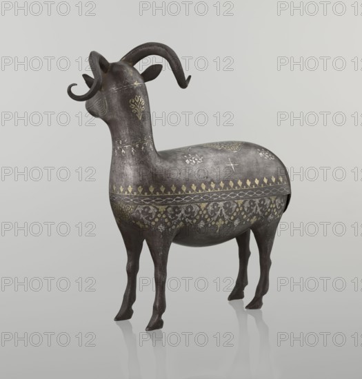 Ram, Islamic art, Persian, Qajar dynasty 1785–1925, sculpture; animal figurine of a ram with horns; decorated on the back with medallions and palmettes with floral ornament; 1st half of the 19th century, Iran; materials not stated; height 22.5 cm, width 20.5 cm, depth 9.0 cm, weight 0.64 kg., A sculptural animal figure with curved horns standing on a reflective surface, rendered in dark gray with a weathered texture and decorated with ornate patterns in gold and lighter gray; the figure has a rounded body, slender legs, stylized ears, and floral and geometric motifs across its neck, sides, and back, with visible highlights and shadowing against a pale gray background.