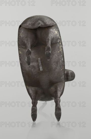 Ram, Persian, Qajar dynasty 1785–1925, 1st half of the 19th century. Sculpture; animal figurine of a ram with horns. Decorated on the back with medallions and palmettes with floral ornament; geometric motifs and floral ornament. Materials/technique: sculpture. Dimensions: height 22.5 cm, width 20.5 cm, depth 9.0 cm; weight 0.64 kg., A dark brown sculptural object resembling an animal is shown from underneath, with a rounded body, four legs extending downward, and a short tail projecting to one side; the surface has worn areas and a few pale gold decorative marks along the flanks and top, and there are areas of lighter brown and grayish patina on the body, set against a pale gray background with a subtle reflection below.