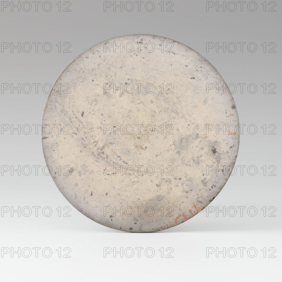 Mirror with TLV decoration on a pedestal in the form of a qilin on a base. Chinese, Qing dynasty 1644–1911. Mirror: cast from chiseled bronze, decoration in flat relief—centrally placed knob enclosed in a square with four T-shaped motifs attached; L- and V-shaped motifs at the edge. Unicorn qilin: cast from chiseled bronze. Base: carved wood. 18th century mirror cast from an earlier product, possibly 6th century–?. Sculpture; mirror. Height 26 cm; diameter 16.2 cm., A large circular object fills most of the image, showing a worn, mottled surface in shades of light gray and off-white with areas of darker gray spotting and smudging; there are small patches of faded rusty orange near the lower edge and subtle hints of beige in places, all set against a smooth gradient background that transitions from medium gray at the top to very light gray at the bottom.