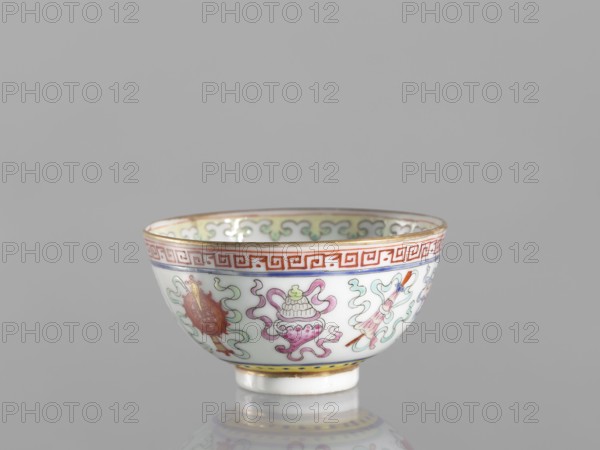 Bowl, ; Qing dynasty 1644–1911, 19th century, China; colored porcelain; bowl on a foot, decorated on the outside with a meander stripe and Buddhist symbols including cranes and endless knot; lambrequin pattern; ceramics; vessel; height 3.6 cm, diameter 6.6 cm., A small porcelain bowl sits on a reflective surface against a plain light gray background. The bowl is primarily white with painted decorative motifs in colors including red, pink, green, blue, yellow, and gold. A red geometric band encircles the rim, and a thin gold line runs along the top edge. Below the rim are flowing cloudlike shapes in pale green and teal, interspersed with stylized objects painted in pink, red, and green with gold highlights. The interior rim shows a repeating cloud scroll pattern in pale green and gold. The foot of the bowl is white with a narrow yellow band above it and a thin gold accent. The bowl casts a soft reflection on the surface beneath it.