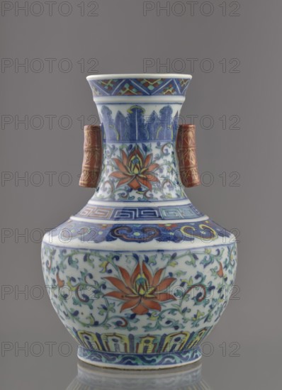 Vase with threads in the shape of bamboo twigs;, Chinese art; Chinese; Qing dynasty 1644–1911, Qianlong period. Ceramics, colored porcelain. Decoration: lotus tendril on the belly, artemisia leaves; lambrequin ornament on the shoulders; geometric and plant borders on the neck; plant motifs. Lotus tendril ornament. Date: 1736–1795. China. Vessel. Height 20 cm; diameter 14.5 cm; weight 0.8 kg., A ceramic vase with a bulbous body and a flared neck standing against a neutral gray background, decorated with intricate floral and foliate patterns in colors including blue, white, orange, green, yellow, and red; the main surface shows stylized orange flowers with green leaves and curling vines on a white ground, bordered by bands of geometric and cloud-like motifs in blue and yellow; the neck features vertical blue leaf-like designs and a band of multicolored diagonal pattern near its rim, while a pair of small cylindrical red handles with gold linear decoration project from the shoulder; the b...