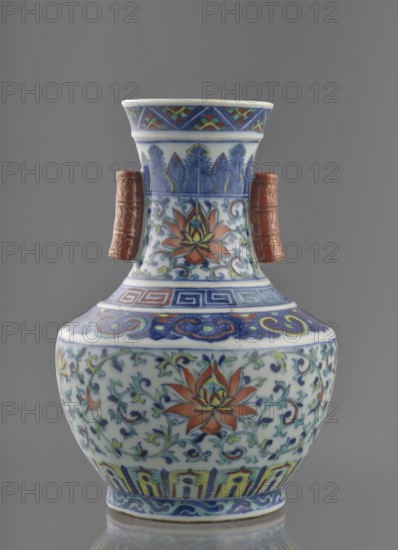 Vase with threads in the shape of bamboo twigs; maker, Chinese, Qing dynasty Qianlong period, 1736–1795. Colored porcelain vessel, height 20 cm, diameter 14.5 cm, weight 0.8 kg. Decoration: lotus tendril on the belly, artemisia leaves; lambrequin ornament on the shoulders; geometric and plant borders on the neck; plant motifs, lotus tendril ornament., A ceramic vase with a rounded body and a narrow neck flares at the rim, decorated with floral and foliate patterns in colors including blue, white, orange, green, yellow, and red; the neck features vertical leaf motifs in blue and green with an orange flower motif below, and there are two short cylindrical handles on the sides in a reddish-brown color with gold detailing; the shoulder and lower body display scrolling vines and stylized flowers in blue, green, orange, and yellow against a white ground, with bands of geometric and wave-like patterns in blue and other colors near the top and base; the piece sits on a reflective surface and t...