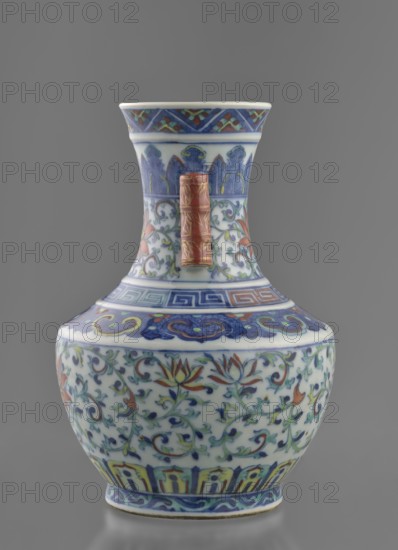 Vase with threads in the shape of bamboo twigs; maker, Chinese; Qing dynasty 1644–1911, Qianlong period 1736–1795; colored porcelain; plant motifs including lotus tendril ornament and artemisia leaves; decoration: lotus tendril on the belly, lambrequin ornament on the shoulders, geometric and plant borders on the neck; vessel; height 20 cm, diameter 14.5 cm, weight 0.8 kg., A ceramic vase with a bulbous body and a flared neck stands against a gray background, decorated with intricate floral and foliate patterns in blue, green, red, yellow, and white; the neck and shoulder feature bands of geometric and stylized motifs in blue and red with accents of green and yellow, and a raised rectangular handle in a reddish-brown color with gold detailing is attached to the neck; the main body shows scrolling vines and lotus-like flowers in shades of blue, green, red, and yellow on a white ground, with additional blue and yellow decorative bands near the base and rim.