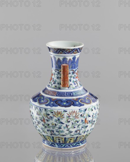 Vase with threads in the shape of bamboo twigs; maker, ; flowers; colored porcelain; Chinese; Qing dynasty, Qianlong period 1736–1795; decoration: lotus tendril ornament, artemisia leaves on the belly; lambrequin ornament on the shoulders; geometric and plant borders on the neck; motifs include bamboos and lotuses, meander and other geometric ornaments; vessel; height 20.0 cm, diameter 14.5 cm., A small ornamental vase with a flared rim and rounded body sits against a plain gray background; the vase is predominantly white with detailed painted floral and foliate patterns in blue, green, and red, with accents of orange and gold; the neck features stylized blue leaf motifs and a patterned band in blue and red near the rim, and a vertical raised handle-like element in metallic gold and reddish tones; the shoulder has a decorative blue band with cloudlike shapes and geometric motifs, while the body displays scrolling vines and lotus-like flowers in blue, green, orange, and red; the base ed...