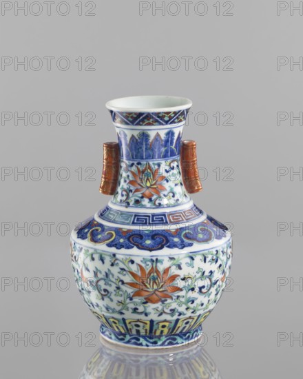 Vase with threads in the shape of bamboo twigs;, colored porcelain; Chinese, Qing dynasty, Qianlong period 1736–1795; decoration: lotus tendril and artemisia leaves on the belly; lambrequin ornament on the shoulders; geometric and plant borders on the neck; motifs: bamboos, lotuses, lotus tendril ornament, meander ornament, geometric ornaments; function: vessel vase; height 20.0 cm, diameter 14.5 cm; inscriptions/notes: flowers., A small decorative vase sits against a neutral gray background, showing a bulbous body with a narrower neck and flared rim, decorated with intricate painted floral and geometric patterns in colors including blue, white, orange, green, yellow, and brown, and featuring two short cylindrical side handles in a brownish-gold tone; the surface displays stylized lotus-like flowers and scrolling vine motifs, bands of geometric fret and cloud-like patterns, and a glossy finish that creates a subtle reflection beneath the vase.