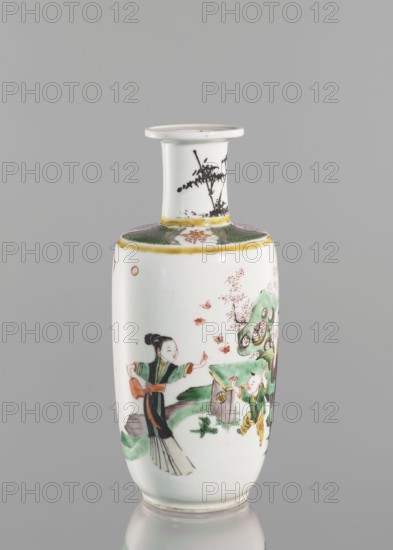 Vase, Chinese, Qing dynasty 1644–1911, 19th century. Colored porcelain vessel with figurative scenes depicting children and women; narrow neck. Height 26.0 cm; diameter 10.5 cm; weight 1.05 kg., A small porcelain vase with a narrow neck and flared rim stands against a gray background; the vase is primarily white with painted scenes in green, black, yellow, red, and orange, including a figure in traditional clothing with black hair and green and black garments, a childlike figure in green and yellow, stylized trees or rocks in green, and scattered small orange shapes; the neck shows a black brushwork plant motif and a band of green and yellow near the shoulder, and the rim and base have subtle yellowish accents.