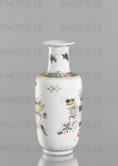 Vase, gift; Chinese; Qing dynasty 1644–1911; ceramics, colored porcelain with hundred antiquities baigu ornament; vase; 19th century; China; height 20.8 cm, diameter 7.5 cm., A white ceramic vase with a narrow neck and flared rim stands against a gray background, decorated with painted motifs in green, orange, yellow, blue, black, and red. The neck shows black leaf-like designs, and the shoulder has a green patterned band with orange floral medallions and a pale yellow border. The body of the vase features a group of painted objects and stylized foliage in green, orange, yellow, blue, and black, including small stands, vessels, and floral elements arranged around the surface. The vase rests on a slightly raised circular base that mirrors the white body.
