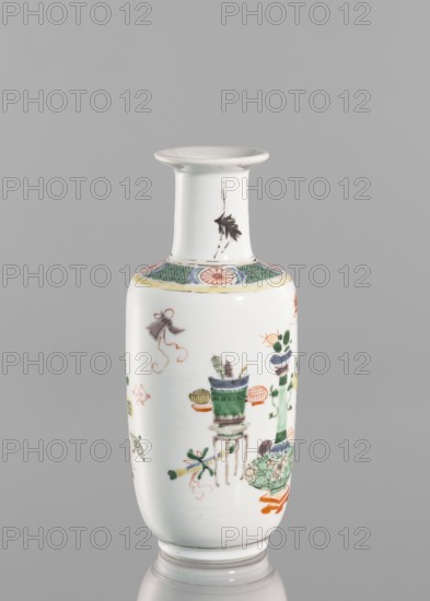 Vase, Chinese, Qing dynasty 1644–1911, 19th century. Colored porcelain vessel decorated with bai gu hundred antiquities ornament. Height 20.8 cm; diameter 7.5 cm., A slender porcelain vase with a flared rim and narrow neck sits against a plain gray background; the vase is predominantly white with painted decorations in green, orange, black, pink, yellow, and blue, including floral motifs, stylized leaves, and objects arranged around the body, a decorative band with green crosshatch and pink circular motifs near the shoulder, and a small black leaf-like mark on the neck.