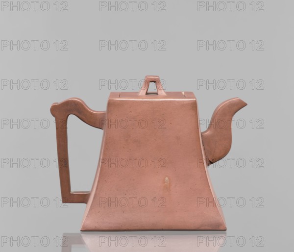 Teapot with a lid; maker, ; used for tea; Harbin, China; ceramics; Chinese art; Chinese culture; Qing dynasty 1644–1911; Yixing style; inscriptions; red-brown stoneware; 19th century; vessel; height 12.2 cm, width 16.3 cm, A trapezoidal teapot with a short square lid and a triangular handle on top, shown in a dusty pinkish-brown color, sits against a smooth light gray background; it has an angular handle on one side and a curved spout on the other, both matching the teapot’s pinkish-brown tone, and the surface shows a few small darker speckles and slight discolorations, with a subtle reflection visible on the glossy surface beneath it.