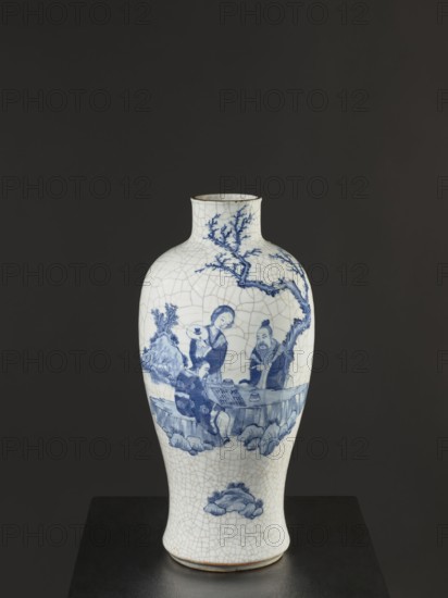 Vase, figurative scenes, ceramics, gardens, Chinese art, Chinese culture, blue-and-white porcelain, games, cracklework decoration, play, Qing dynasty 1644–1911, 18th–19th century Jiaqing period, 1797–1820, China, vessel, height 54.5 cm, width 9.8 cm, A tall ceramic vase with a white base and a crackled glaze surface, decorated in blue with a scene of a group of people seated at a low table beneath a tree branch, surrounded by stylized rocks and foliage; the vase has a narrow neck with a slight lip and a rounded body tapering to a narrower foot, and it sits on a dark platform against a dark gray background.