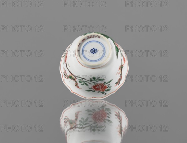Bowl, ceramic vessel, colorful porcelain in Kangxi style Kangxi period, 1662–1722, Qing dynasty 1644–1911. Decorated with floral motifs, plum trees and bird images. China; height 5.4 cm, diameter 8.8 cm., A white porcelain bowl with scalloped edges sits upside down on a reflective gray surface, showing painted floral and bird motifs in red, green, and black with blue circular detail at the base and a reflection of the bowl visible below; the background is gray.