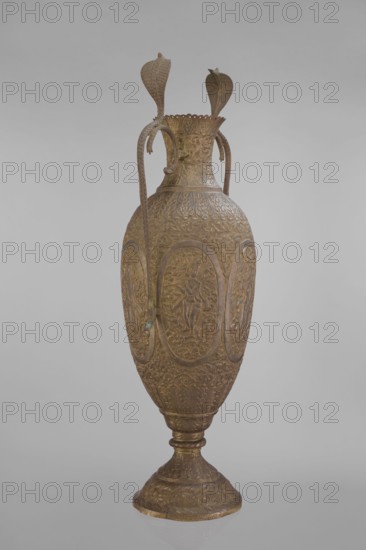Vase, repossession; Vishnu, cobras snakes, plant ornament, geometric ornament, figural scenes, fish, halos, maces, religion, snakes, processions, flutes, clubs. On the belly six ovoid reserves with figural decoration four female figures with wreaths, two images of Vishnu; plant and animal motifs on the entire surface. 19th century, India; vessel. Height 65.0 cm, width 27.5 cm, weight 2.95 kg., A tall ornate metal vessel stands upright against a plain light gray background, rendered in warm brass and bronze tones with areas of darker brown patina; the vase has an elongated oval body rising from a flared round base with decorative ridges, and the surface is covered in intricate raised floral and foliate patterns with repeating oval medallions that contain human-like figures in bas-relief; two long curved handles extend from the neck to the shoulder, each handle shaped like a stylized serpentine form terminating in broad flattened fin-like elements, and the neck flares into a scalloped ri...