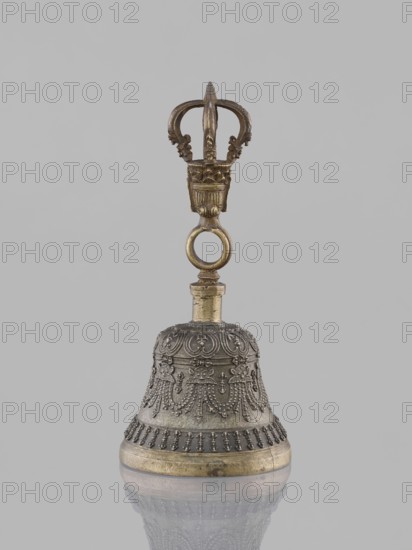Bell ghanta, 19th century, Tibet. Ritual object used in Tibetan Buddhist religious rites; percussion idiophone. Bronze bell with bowl decorated in the form of festoons; associated vajra/heads, mantras inscribed. Height 18.7 cm, width 8.5 cm., A single ornate metal bell with a decorative handle is centered against a plain light gray background; the bell shows detailed raised patterns and bead-like embellishments and has a rounded base with a band, while the handle above features a ring and a crown-like top with sculpted flourishes, all rendered in metallic tones of gold, brass, and dark gray.