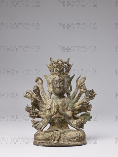 Cundi, unknown sculptor; gift; Chinese/Tibetan; Qing dynasty 1644–1911, 18th–19th century; Buddhist sculpture of the bodhisattva Cundi; materials not specified; iconography includes lotuses, mudras, sutra, fish, goddesses, protective deities; height 24.3 cm, width 22.0 cm, weight 3.38 kg; related to Chinese and Tibetan Buddhism., A small bronze statue of a seated multi-armed figure with a crown, shown against a plain gray background; the figure sits cross-legged on a rounded base with draped robes, hands held in various mudras and holding small objects, and several arms fanning out behind it; the crown is ornate and rises above the head, which has a calm facial expression and elongated earlobes; the surface shows a mottled patina with green and brown tones and areas of darker bronze.