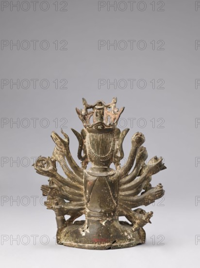Cundi, unknown sculptor; Chinese/Tibetan Buddhist sculpture, Qing 1644–1911, 18th–19th century; subject: Cundi bodhisattva, Buddhist art—Chinese Buddhism, Tibetan influence; materials/technique: sculpture; iconography: lotuses, mudras, sutra, fish, goddesses, protective deities; dimensions: height 24.3 cm, width 22.0 cm, weight 3.38 kg; possible place of origin: China, Tibet; inscriptions/marks: none noted., A sculptural object viewed from the back showing a central figure with a crownlike element at the top and a hair or headdress detail with vertical lines; multiple curved limbs or appendages fan outward from the central body, many ending in handlike shapes; the base is rounded and worn with surface irregularities and chipped areas; the surface finishes include muted brown, dark green, and patches of lighter beige or off-white where the material is worn, with small areas of reddish discoloration; the background is a uniform light gray.