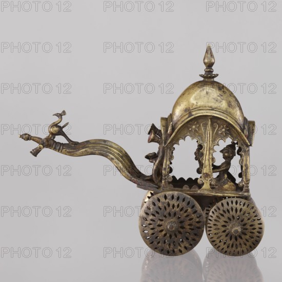 Miniature of a chariot;, 19th century, India. Model of a temple chariot showing a bird peacock perched on a bow-shaped shaft; under a canopy topped with a pike sit figures including Krishna feeding on butter; in front, in the driver's seat, there is also Krishna. Height 24.0 cm; width 28.0 cm., A small ornate metal cart with a domed canopy and a pointed finial, shown against a light gray background, rendered in aged gold and dark bronze tones. The cart has a long curved shaft ending in a decorative finial shaped like a bird, with the shaft and bird in gold and darker patina. The canopy is arched with scalloped openings and ornamental edgework, revealing a seated human figure inside rendered in dark bronze. The cart rests on a pair of large circular wheels with perforated floral-like patterns in darker bronze, and the surfaces show areas of wear and mottled discoloration in gold and brown. The overall colors visible are gold, bronze, brown, and gray.