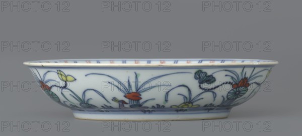 Plate, Paderewski, Ignacy Jan 1860-1941 provenance, Chinese art, Chinese culture, Qing dynasty 1644–1911, colored porcelain, decoration with lotuses and ducks in mirror and outside, 1st half of the 18th century, China; vessel; height 3.5 cm, diameter 15.8 cm, A shallow porcelain bowl shown in profile with a smooth pale background and hand-painted floral and foliage motifs in blue, green, yellow, and red; the rim has a thin unpainted band and the interior edge shows alternating short vertical strokes in muted red and blue; the exterior decoration includes flowing blue outlines of leaves and stems, stylized blossoms in red and yellow, and shaded green leaves, all sitting above a narrow blue band near the foot; the overall colors visible are white, blue, green, yellow, red, and a touch of beige on the base edge.