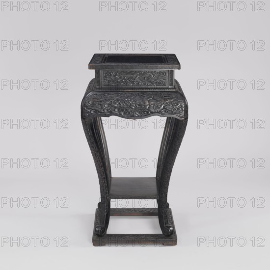 Table, phoenixes and dragons iconography, Chinese art, Chinese culture, Qing 1644–1911, 19th century, furniture, piece of furniture, height 77.0 cm, width 41.0 cm, depth 36.6 cm, A dark wooden stand with intricate carved ornamentation, showing a rectangular top section perched on a scalloped apron decorated with swirling carved motifs, supported by a pair of curved carved legs that descend to a rectangular base with a lower shelf between them; the visible colors are dark brown to near-black wood with subtle lighter brown highlights and a pale gray background.