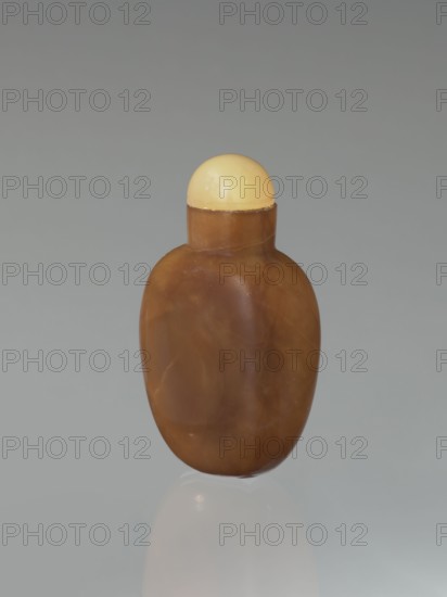 Snuffbox, Chinese, Qing dynasty 1644–1911, 19th century, vessel; height 6.8 cm, width 4.0 cm, depth 2.4 cm., A small rounded bottle with a smooth brown body and a pale yellow rounded cap sits against a soft gray background, the bottle showing subtle lighter and darker brown marbling and a faint reflection beneath it.