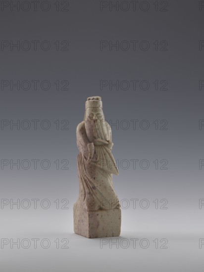 Sage with a Fan, figurine of a man holding a fan, Chinese art, fans, Chinese culture, Qing dynasty 1644–1911, 19th century, China, sculpture; height 16.1 cm, width 4.4 cm, depth 4.3 cm, A carved stone figure stands on a square base, showing a robed person with a long beard and a rounded hat, the form displaying flowing drapery folds and a hand raised to the face; the sculpture is mottled with pale beige and light brown tones with darker brown speckles, set against a smooth gradient background of dark gray at the top fading to light gray at the bottom.