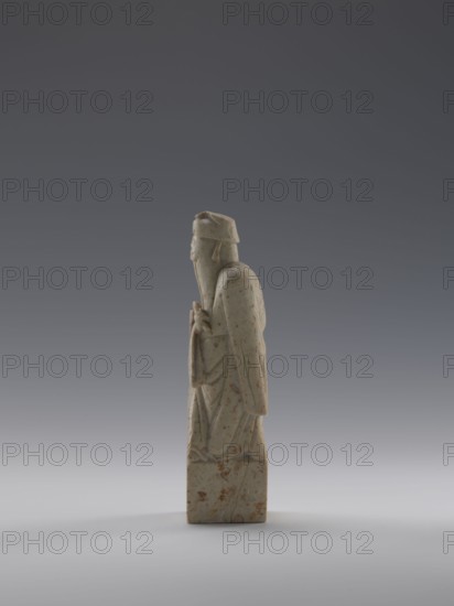 Sage with a Fan, figurine of a man holding a fan, Chinese, Qing dynasty 1644–1911, 19th century, sculpture; height 16.1 cm, width 4.4 cm, depth 4.3 cm., A pale stone figurine stands upright on a rectangular base against a gradient gray background, showing a carved figure draped in long flowing robes and wearing a cap; the stone is off-white with brown and reddish speckles and patches, the carving displays smooth rounded contours with folded garment details and a long beard, and the overall scene includes shades of gray in the background and a subtle shadow on the pale surface below the base.