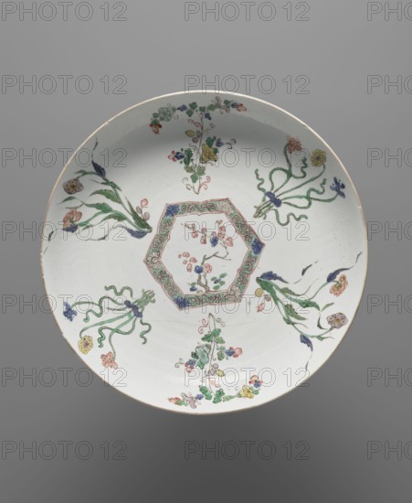 Platter, Chinese, Qing dynasty 1644–1911, 19th century; colored porcelain with floral decorations and floral ornaments; signed; vessel; height 4.3 cm, diameter 27 cm., A round ceramic plate with a white background decorated with a central hexagonal cartouche containing delicate floral sprigs and a patterned border, surrounded by several stylized floral motifs and flowing ribbonlike stems placed around the inner field; the painted colors visible include green, blue, pink, yellow, red, and purple, with thin dark outlines and subtle shading on the leaves and petals, and a plain rim with a light beige edge.