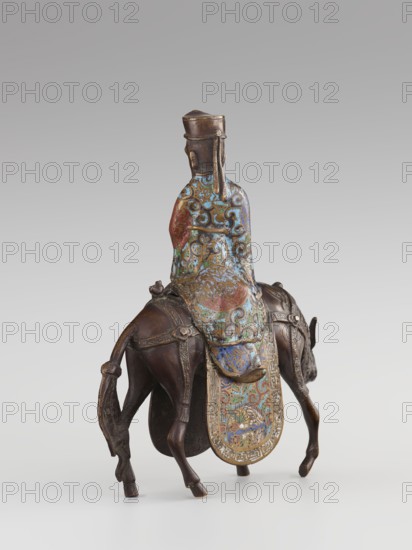 Sage on a Mule, cloisonné enamel, Qing 1644–1911, 19th century, China; sculpture depicting a sage riding a mule; materials and motifs: cloisonné enamel with meander ornament, plant motifs, scrolls, zoomorphic motifs, birds; figurative depiction of men/mules; dimensions: height 26.0 cm, width 25.5 cm, depth 6.0 cm., A sculpted figure seated on an animal viewed from behind, with the figure wearing a tall headpiece and a long flowing robe covered in ornate swirling patterns in blue, green, red, and gold tones; the animal appears dark brown with carved tack and a decorative cloth draped over its back that echoes the figure's colorful patterns, showing similar blue, green, red, and gold hues; the overall surface shows metallic bronze and aged patina in brown and bronze shades against a plain light gray background.